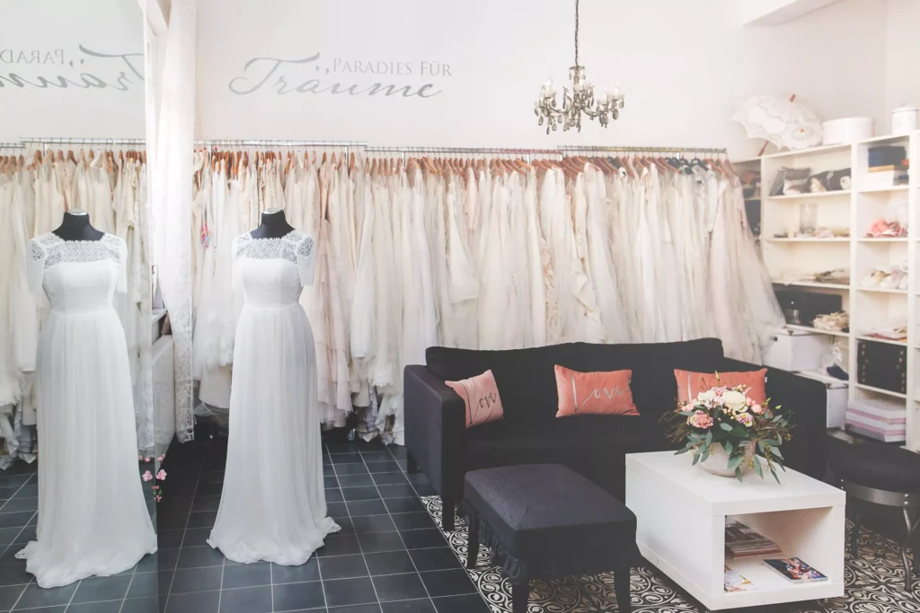 Brautmodengeschäft in Stuttgart mit schöner Brautmode und Brautkleidern aus zweiter Hand - zwei weiße Brautkleider auf Schaufensterpuppen, ein schwarzes Sofa und Regale mit Accessoires, um Ihr perfektes gebrauchtes Traumkleid zu finden.