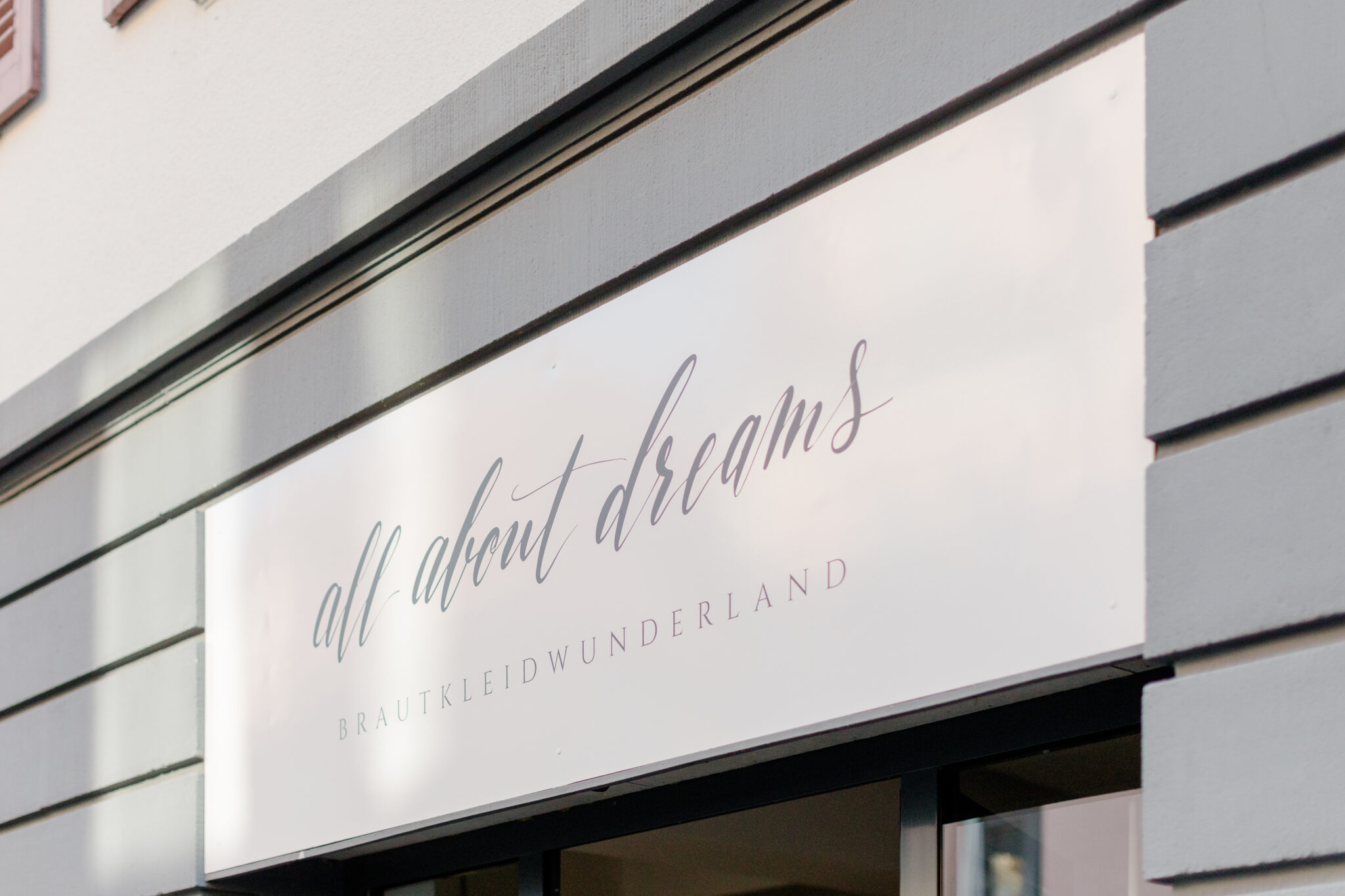 Auf einem Ladenschild steht in stilvoller Schreibschrift auf weißem Hintergrund alles über Träume BRAUTKLEIDWUNDERLAND - entdecken Sie nachhaltige Brautkleider und Pre-loved Traumkleid-Highlights bei Brautmode in Stuttgart.