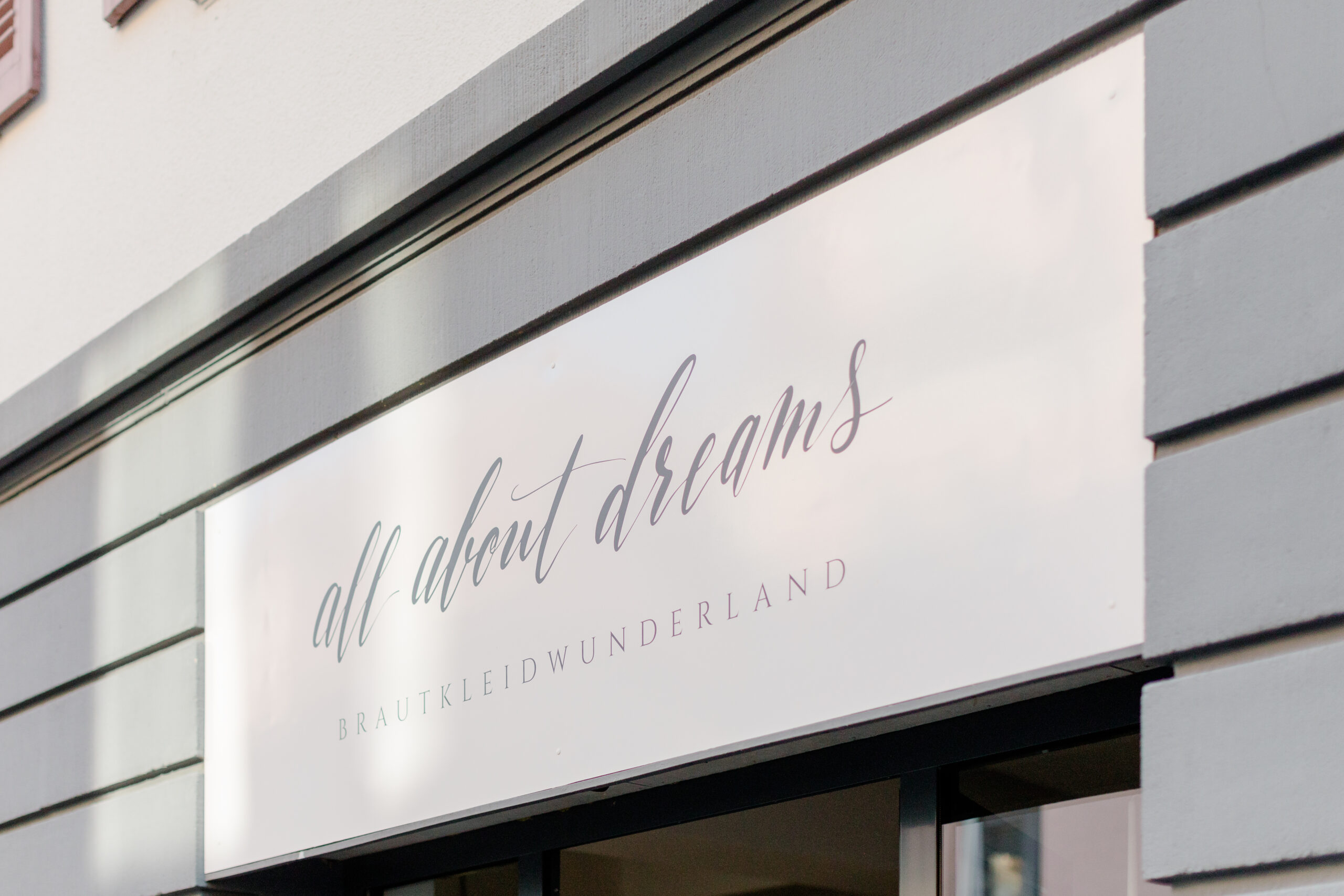 Auf einem Ladenschild steht in stilvoller Schreibschrift auf weißem Hintergrund alles über Träume BRAUTKLEIDWUNDERLAND - entdecken Sie nachhaltige Brautkleider und Pre-loved Traumkleid-Highlights bei Brautmode in Stuttgart.