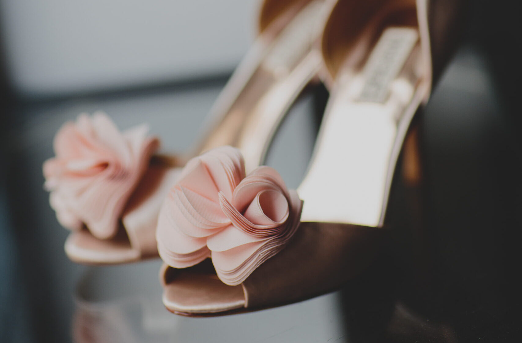 Nahaufnahme von eleganten High Heels mit rosafarbener Stoffblumenverzierung an den Zehen, perfekt um Ihren Brautlook zu vervollständigen. Entdecken Sie einzigartige Accessoires wie diese in Second Hand Brautkleider Shops für Brautmode in Stuttgart.